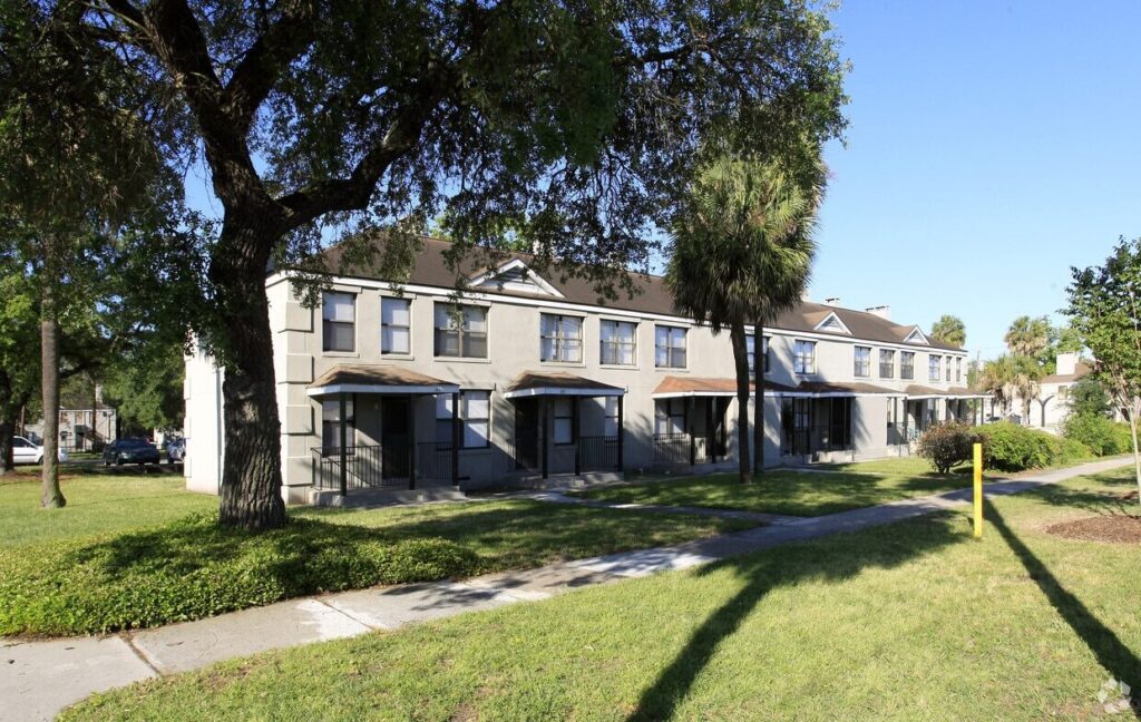 Row of two-story gray apartment buildings at Yamacraw Village in Savannah, Georgia, with large trees, sidewalks, and grass in front.