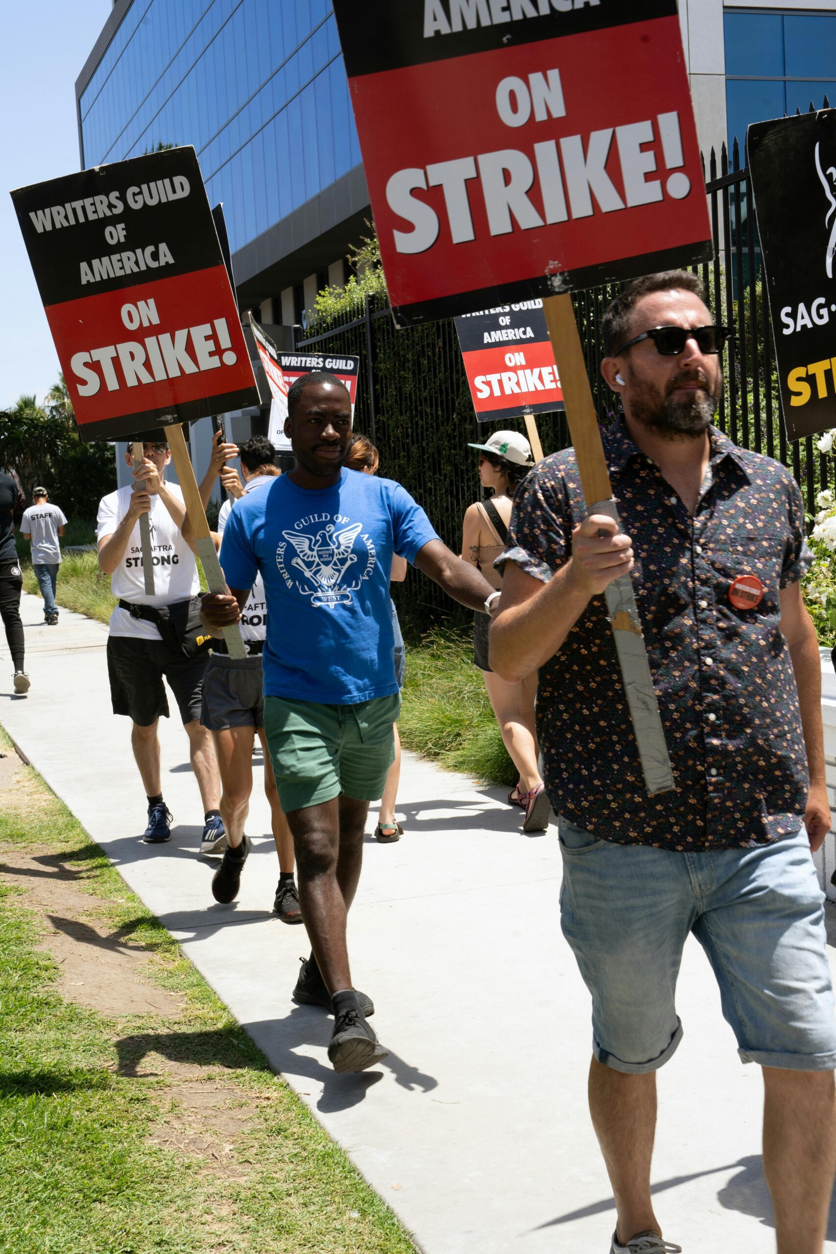 Protesters holding signs during a Writers Guild of America strike on an urban sidewalk.