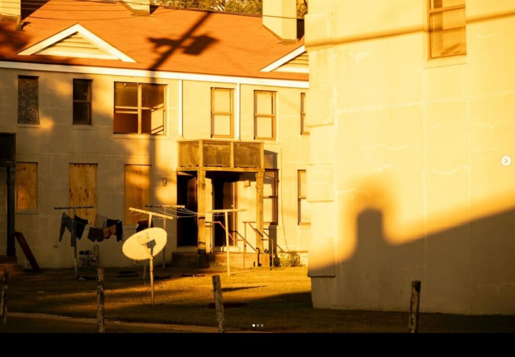 Apartment building at Yamacraw Village in golden light, with a clothesline, satellite dish, and long shadows across the yard.